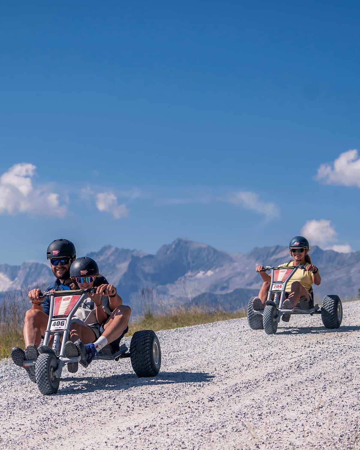 Familie genießt die rasante Abfahrt mit Mountaincarts auf der 4 km langen Strecke in der Wildkogel-Arena – actionreicher Outdoor-Spaß im Sommer mit Ausblick auf die Gipfel der Hohen Tauern.