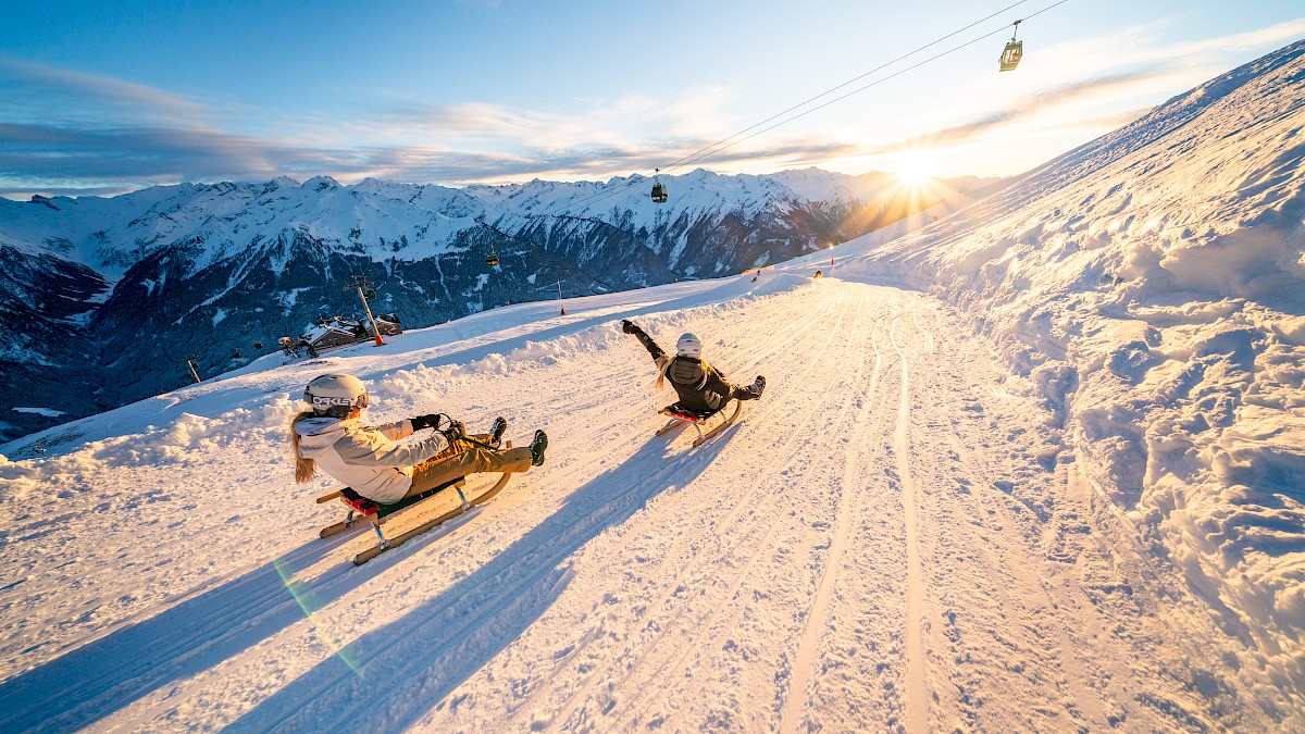 Rodelspaß auf der längsten beleuchteten Rodelbahn der Welt in der Wildkogel-Arena, 14 km Wintervergnügen mit Panoramablick auf die Hohen Tauern bei Sonnenuntergang.
