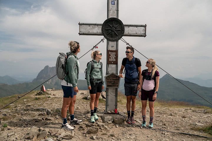 Four hikers reach the summit in the Wildkogel Arena and gather around the impressive summit cross with views of the Großer Rettenstein – an unforgettable hiking moment in SalzburgerLand.