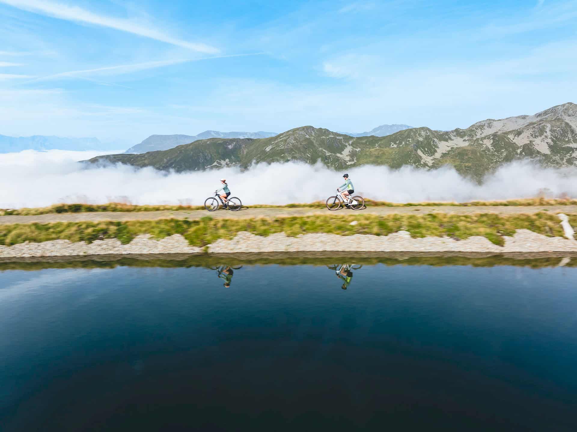 Zwei Radfahrer genießen eine Panorama-Tour entlang eines klaren Bergsees mit Blick auf die Kitzbüheler Alpen in der Wildkogel-Arena Neukirchen & Bramberg.