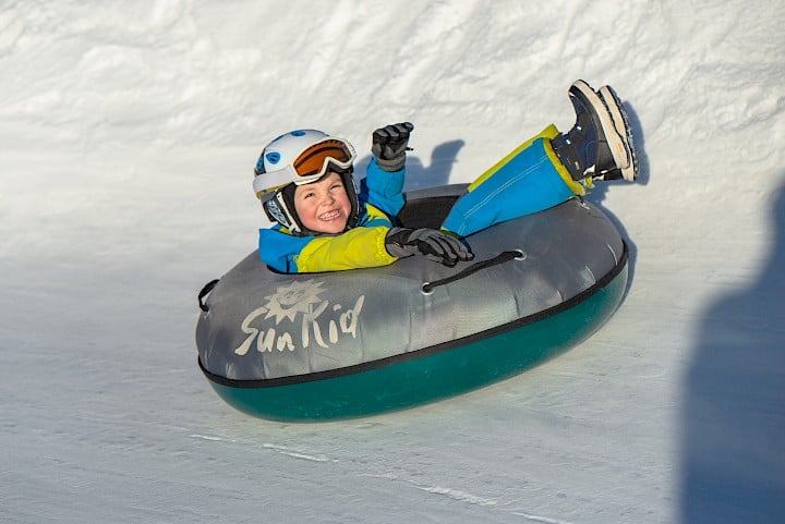 Smiling boy snow tubing in the Wildkogel Arena – winter fun on a groomed tubing track with inflatable sled.