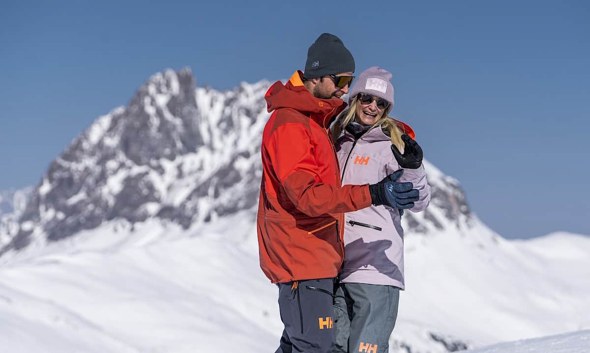 A smiling couple dances a traditional "Snow Waltz" in the sunshine against a stunning alpine winter backdrop. Dressed in warm ski clothes, they enjoy this romantic moment on the snowy mountain – inspired by the “Snow Waltz Package”.